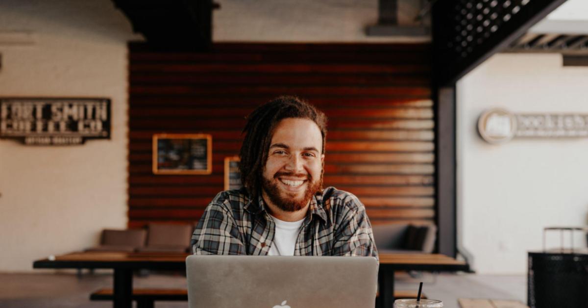 A imagem mostra um homem pardo, de cabelos ruivos em dreads. Ele está sentado de frente para um computador, como referência a uma pessoa empreendedora que usa inteligência artificial em seu negócio.