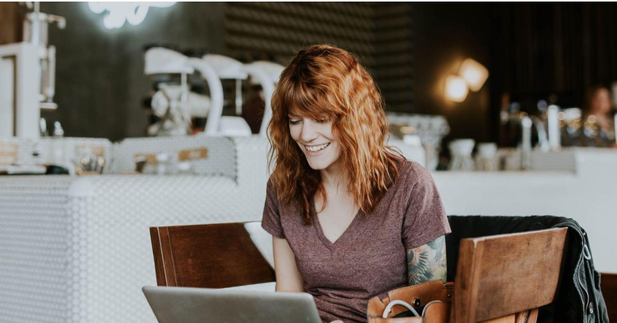 A imagem mostra uma mulher branca, de cabelos ruivos em. Ela está sentada de frente para um computador, como referência a uma pessoa empreendedora que faz a gestão financeira do seu negócio.