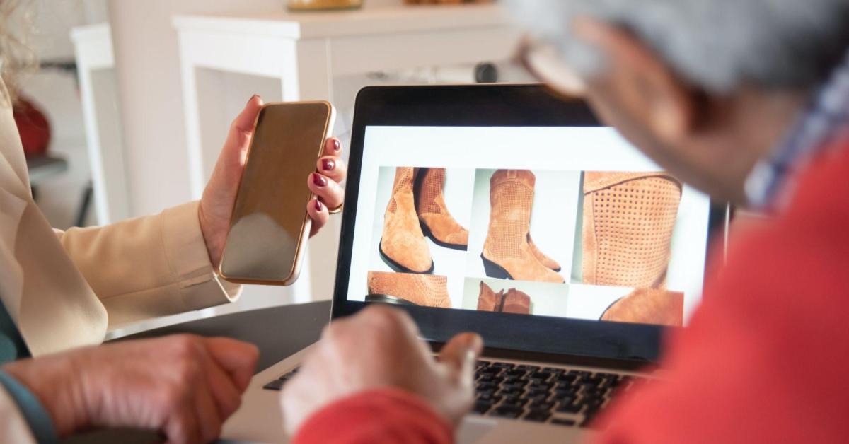 A imagem mostra duas pessoas observando um site de botas marrons. Uma alusão ao fato de que fotografias são essenciais para uma loja online.