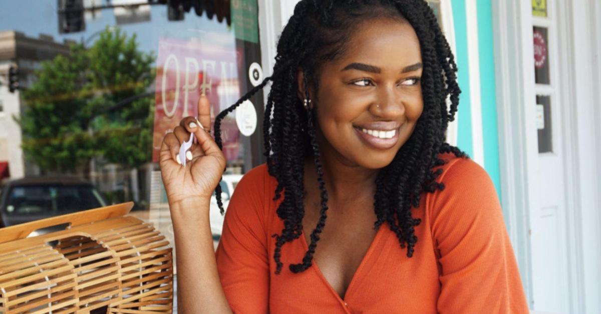 Uma mulher preta, de dreads, veste uma blusa laranja, e sorri para algo que não vemos na tela. Ela representa uma consumidora considerada público-alvo para empreendedores que pensam em vender no verão
