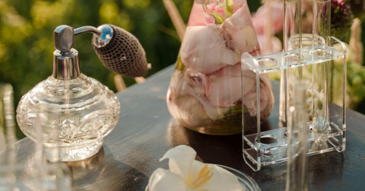 A imagem mostra uma mesa com vidros de perfumes e algumas flores rosas sobrepostas, um exemplo de produtos frágeis.