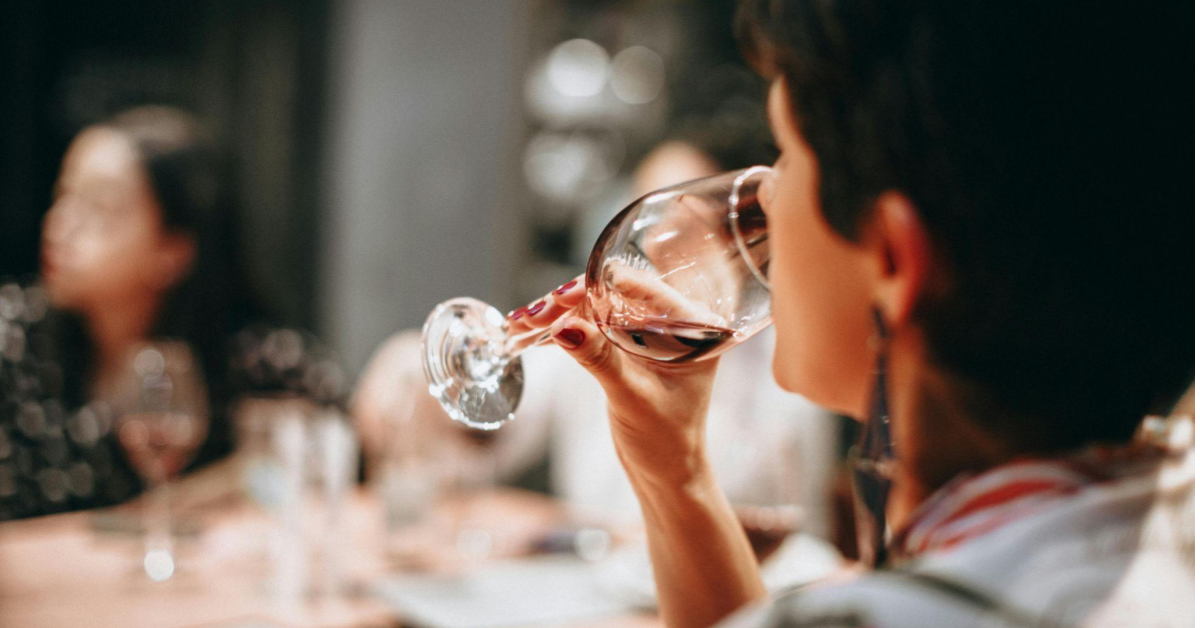 A imagem mostra uma mulher bebendo uma taça de vinho, uma alusão a um transporte de vinho bem feito pelo e-commerce.