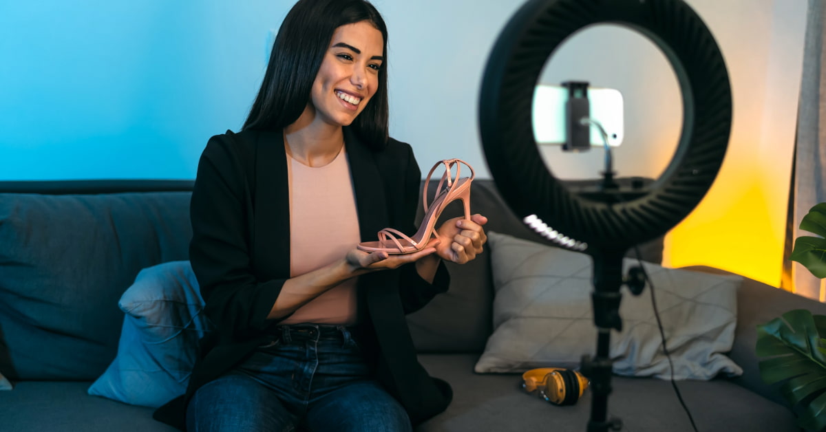 Mulher se filmando com um celular e um ring light enquanto mostra um sapato representando como ganhar dinheiro no Instagram