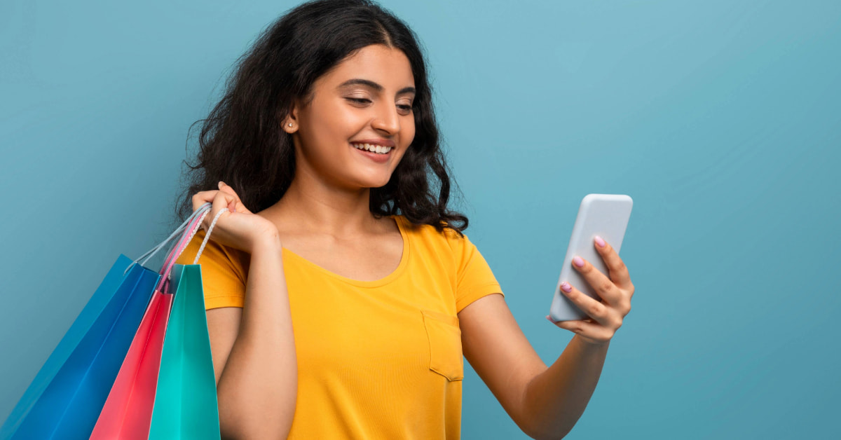 Mulher sorridente com sacolas olhando para o celular representando como aumentar as vendas pelo whatsapp
