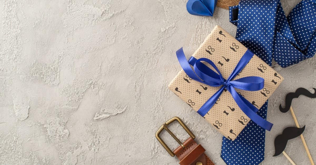 Ideias de presente Dia dos Pais com gravata azul, cinto de couro e caixa de presente decorada com laço.
