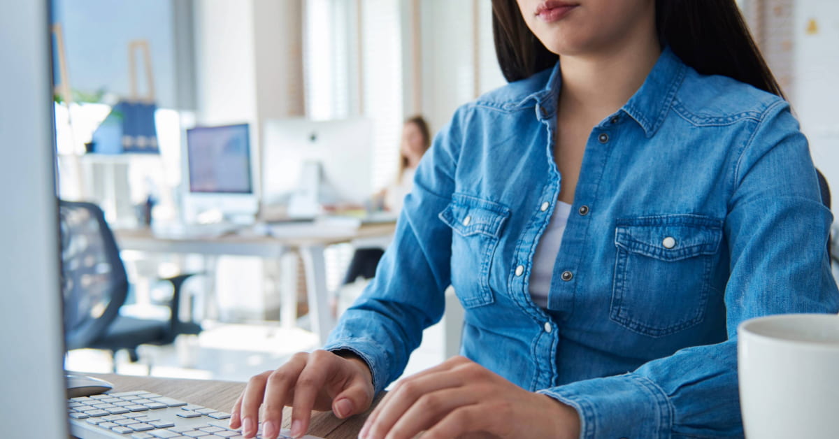 Empreendedora digitando no computador enquanto cria texto pronto para divulgação de loja virtual em um ambiente de escritório.