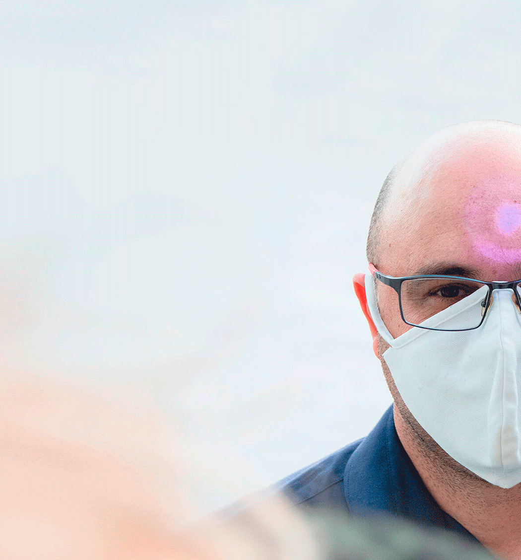 Homem branco de óculos e de máscara tendo a sua temperatura medida
